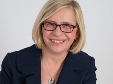 Professional headshot of a woman with short blonde hair looking at the camera with a slight smile and red glasses