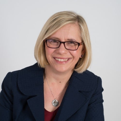 Professional headshot of a woman with short blonde hair looking at the camera with a slight smile and red glasses