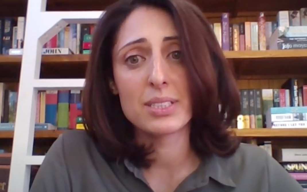 A woman with shoulder-length brown hair and a green shirt sits in front of a bookshelf filled with books, looking slightly concerned. A white ladder leans against the shelves in the background.