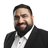 A man with short black hair, a beard, and mustache, wearing a white dress shirt and a black suit jacket, smiling at the camera against a white background.