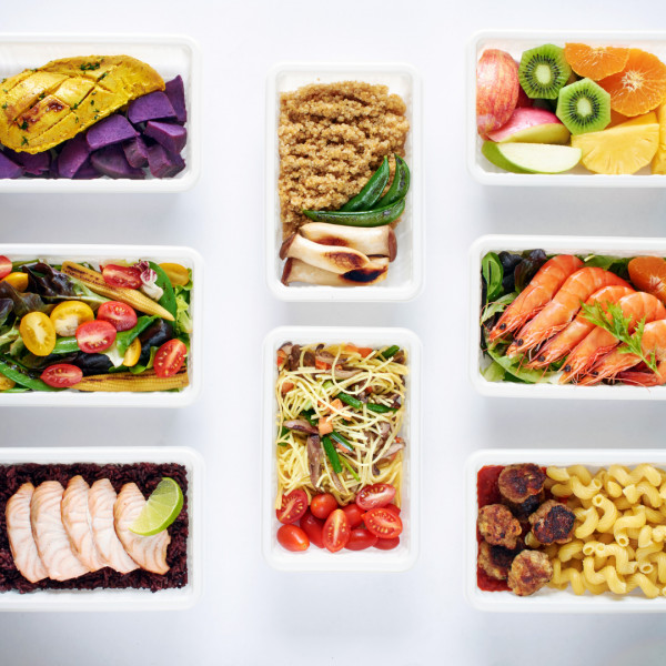 A variety of healthy meal prep containers with foods including grilled chicken, shrimp, pasta, salads, vegetables, fruits, noodles, and quinoa, neatly arranged on a white background.