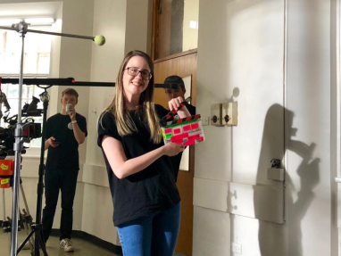 A woman holding a box in a room with other people behind her.