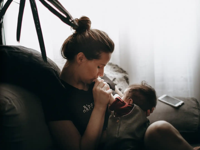 mother holding baby and at home, kissing its hand