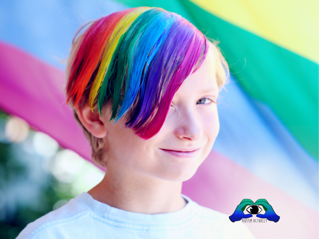 A smiling child with rainbow-coloured hair stands in front of a brightly coloured pride flag. The child is wearing a white shirt, and there’s a small “Autism Actually” logo in the corner of the image.