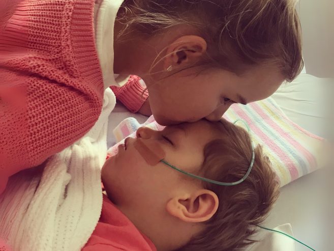 sister kissing her brother who is in hospital bed