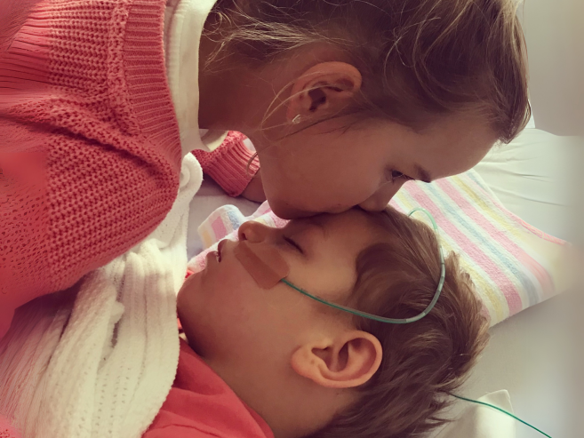 sister kissing her brother who is in hospital bed