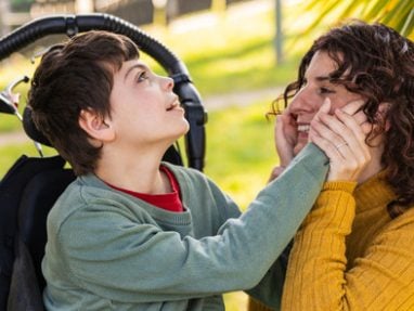 Young boy in wheel chair touching his mothers face