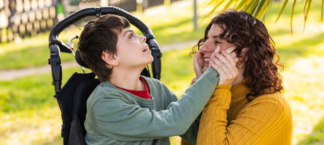 Young boy in wheel chair touching his mothers face