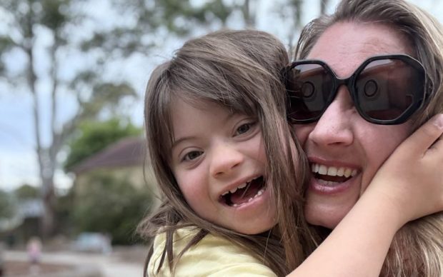 woman with sunglasses smiling at camera as daughter hugs her